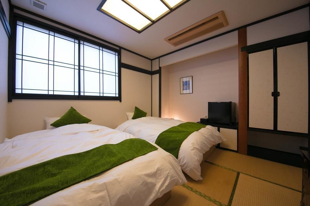 Une pièce de style japonais traditionnel, avec un sol recouvert de tatamis, deux lits aux accents verts, une télévision et une porte coulissante.