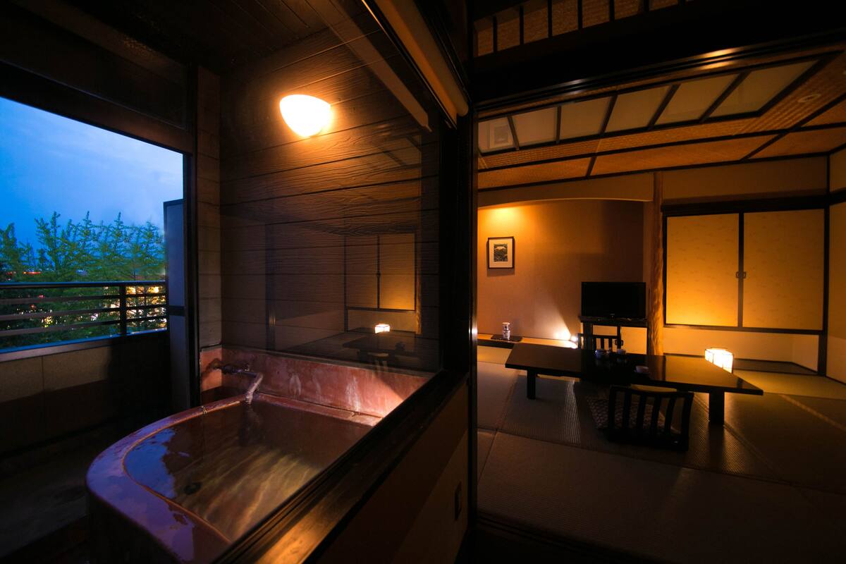 A traditional Japanese room with tatami flooring, a wooden bathtub, and a low table with a television.