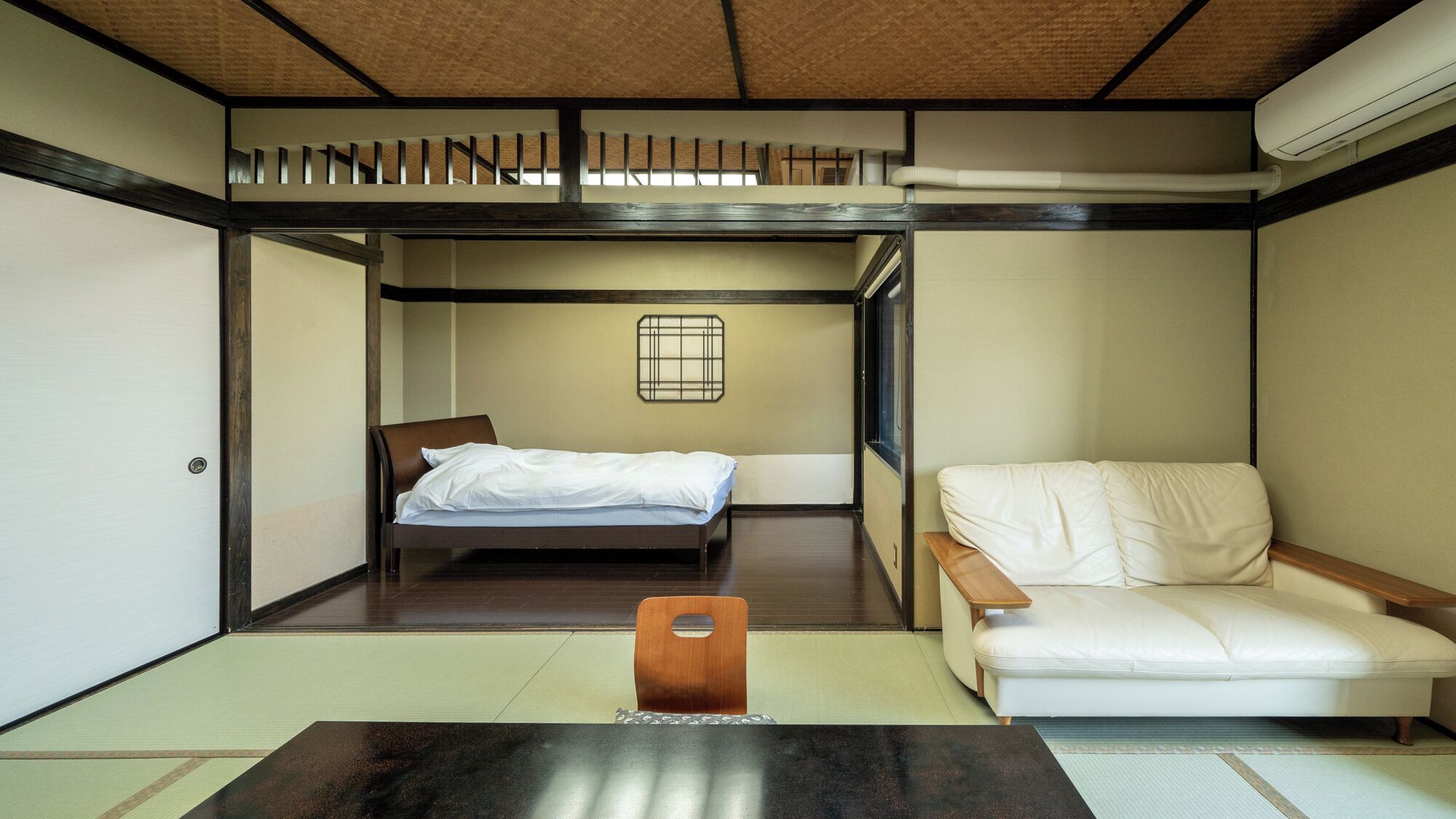 Une pièce de style japonais traditionnel, avec un sol recouvert de tatamis, un lit bas, un canapé et une petite table.