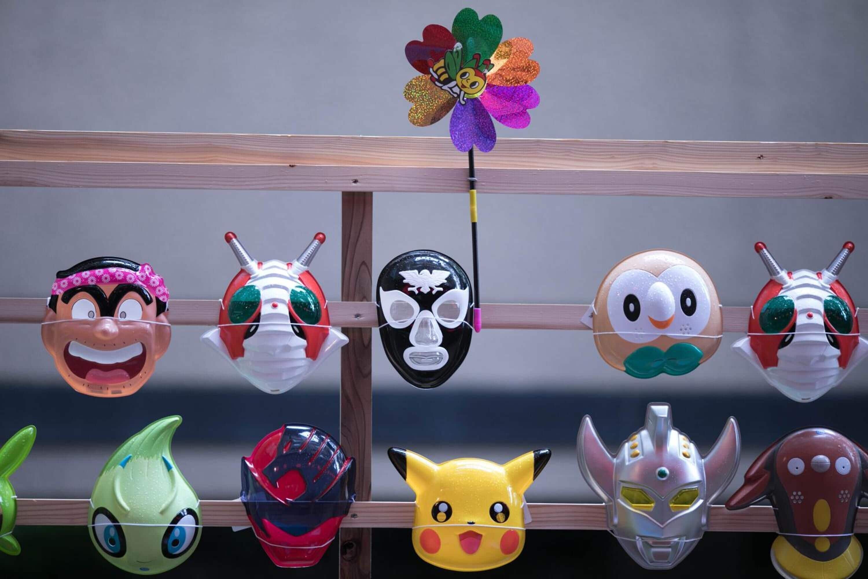 A collection of various character masks hanging on a wooden rack.
