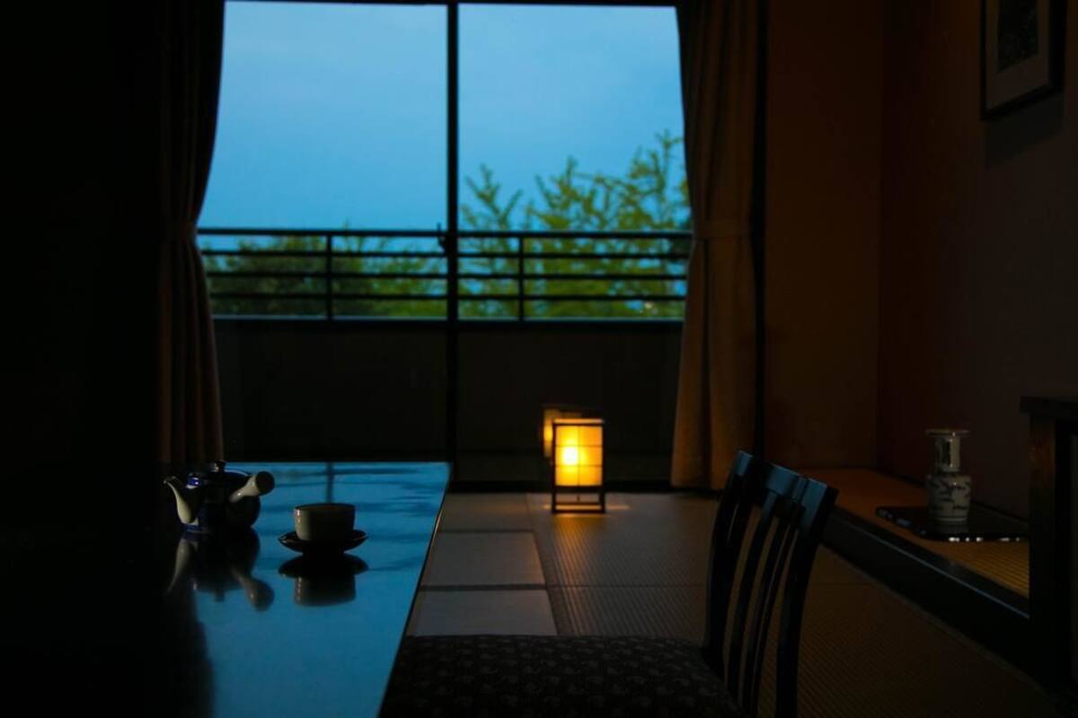 A dimly lit room with a table and chairs, a teapot, and a cup. A lantern provides light in the center.