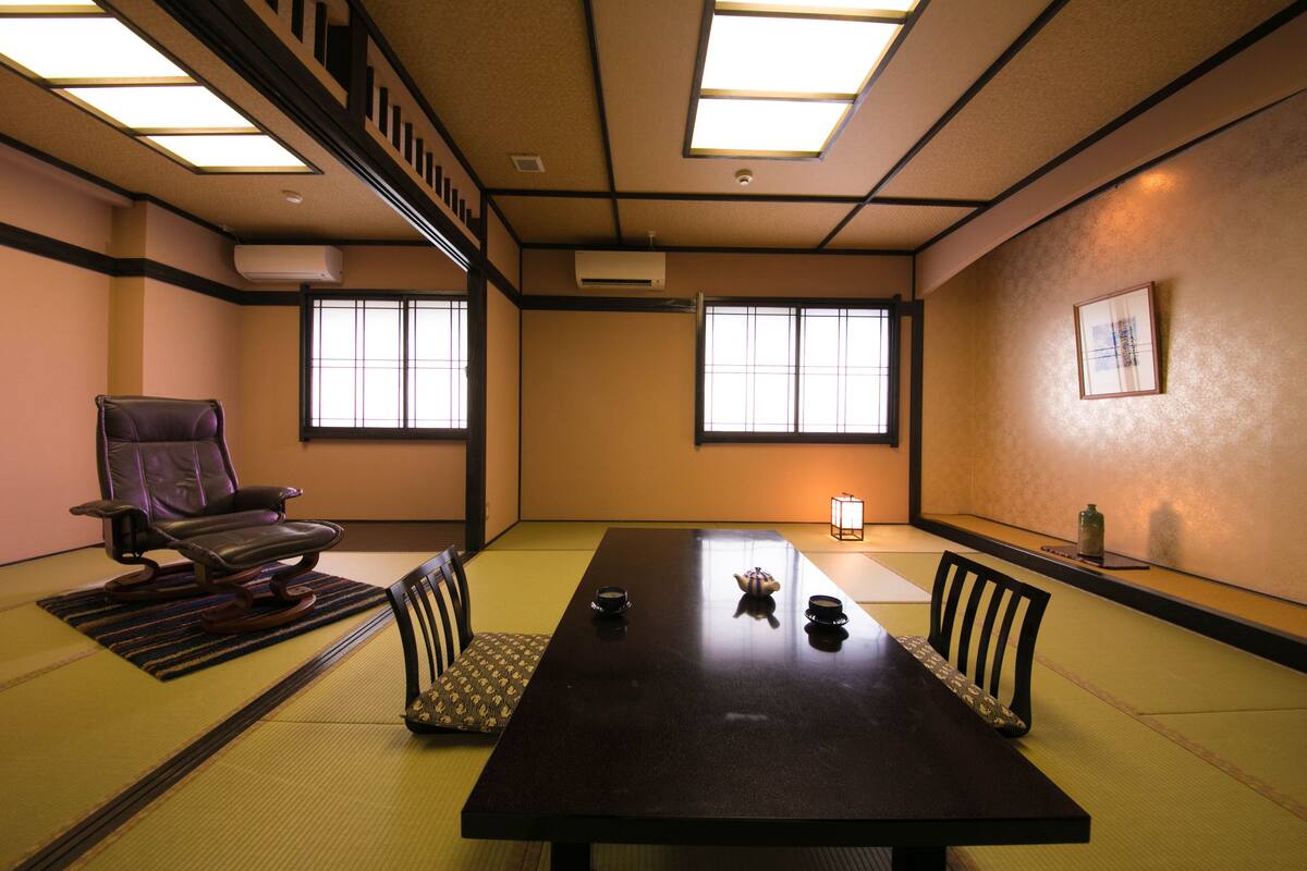A traditional Japanese meeting room with tatami flooring, a low table, and a cushioned chair.