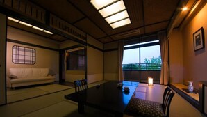 Ett traditionellt japanskt rum med tatamimattor på golvet, ett lågt bord, en soffa och ett fönster med utsikt över grönskan.