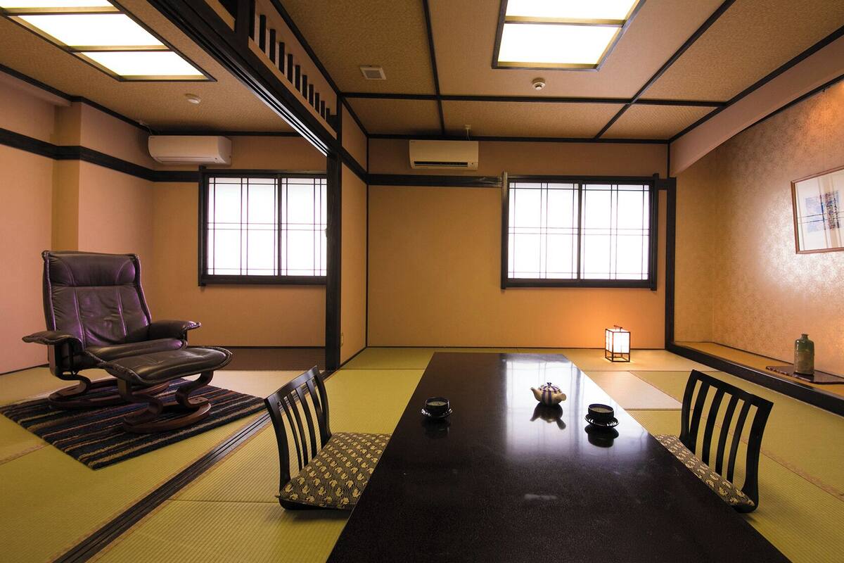 A traditional tatami room with a low table, tatami mats, a black leather chair, and a shoji screen window.