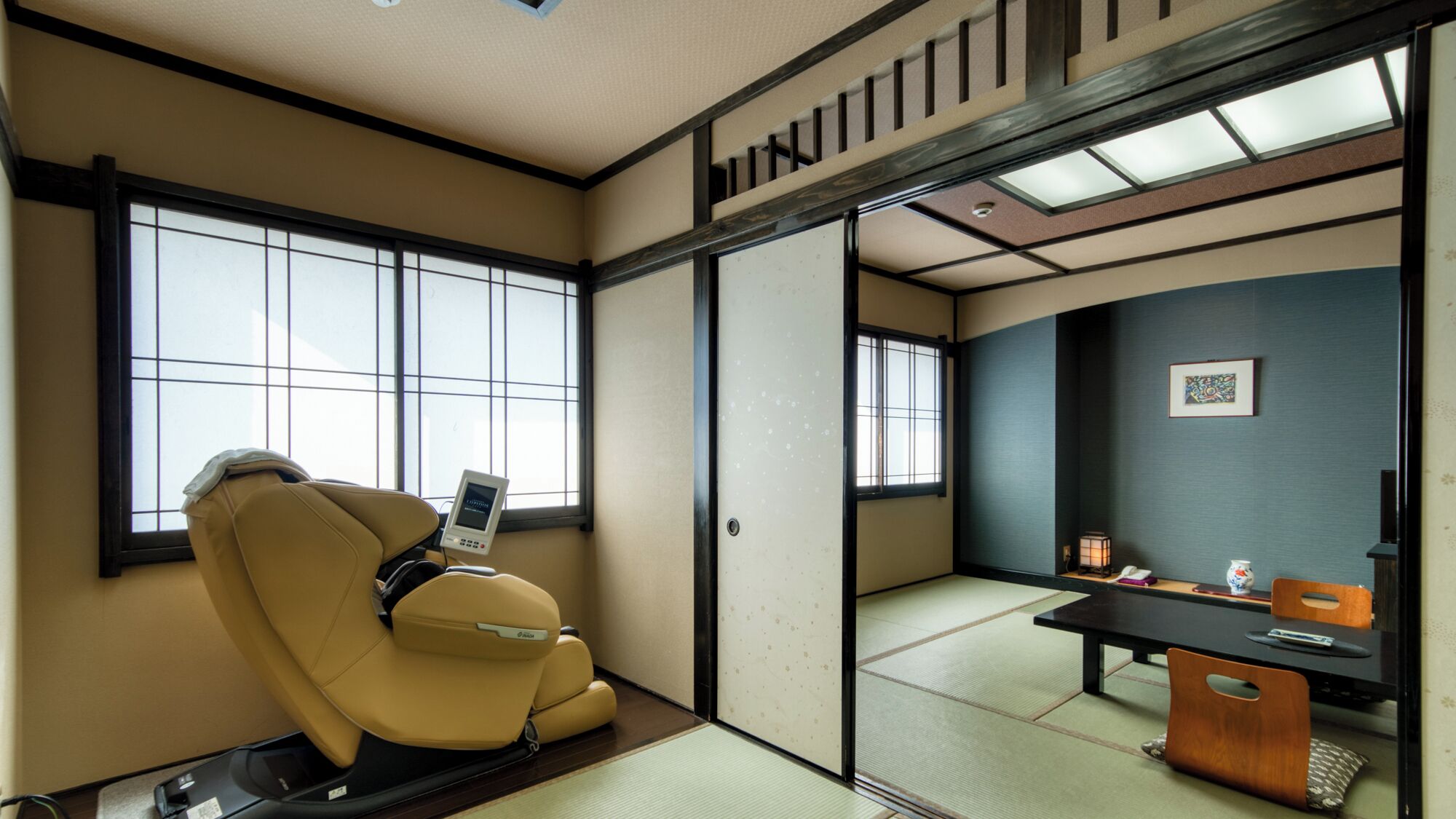 Una habitación japonesa tradicional con suelo de tatami, un sillón de masajes, un escritorio con lámpara y una puerta corredera.