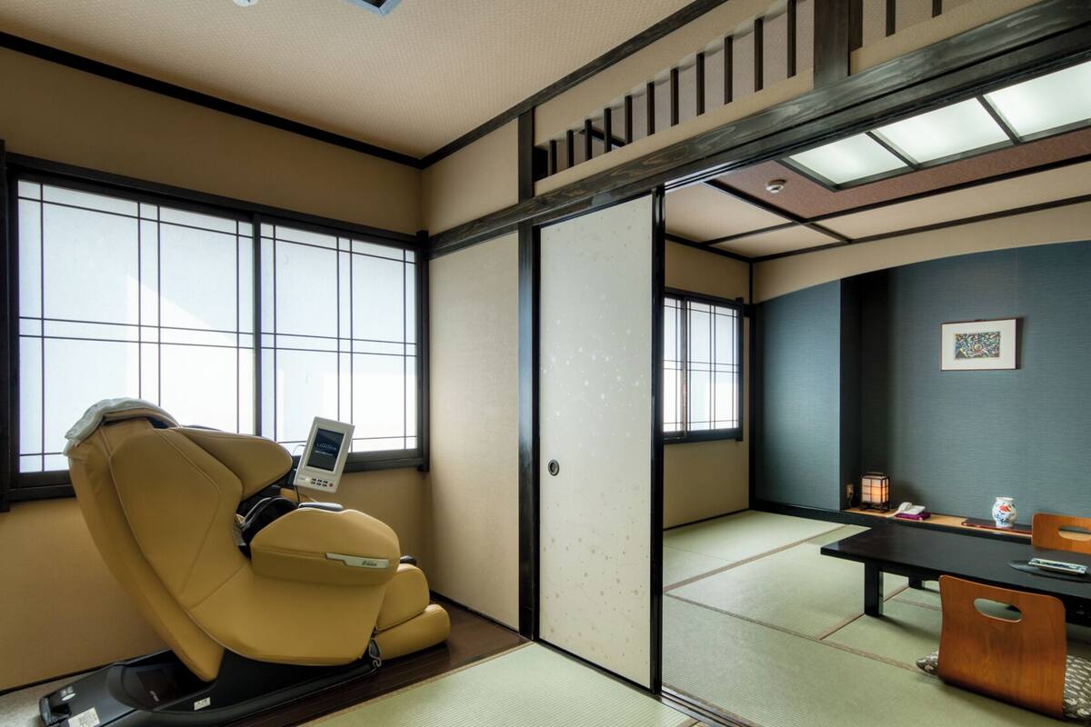 A traditional Japanese room with tatami flooring, a massage chair, a desk with a lamp, and a sliding door.