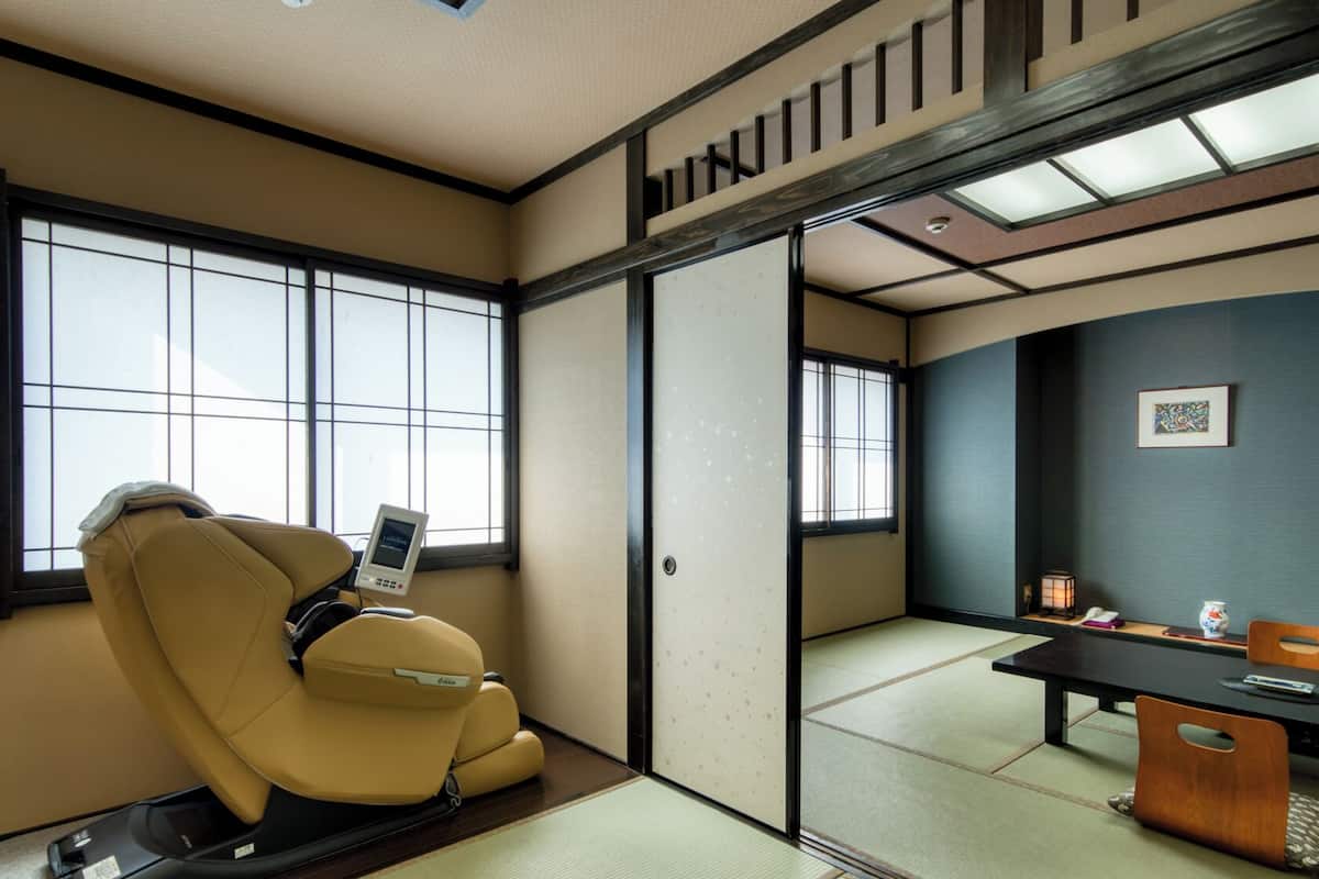 Una habitación japonesa tradicional con suelo de tatami, un sillón de masajes, un escritorio con lámpara y una puerta corredera.