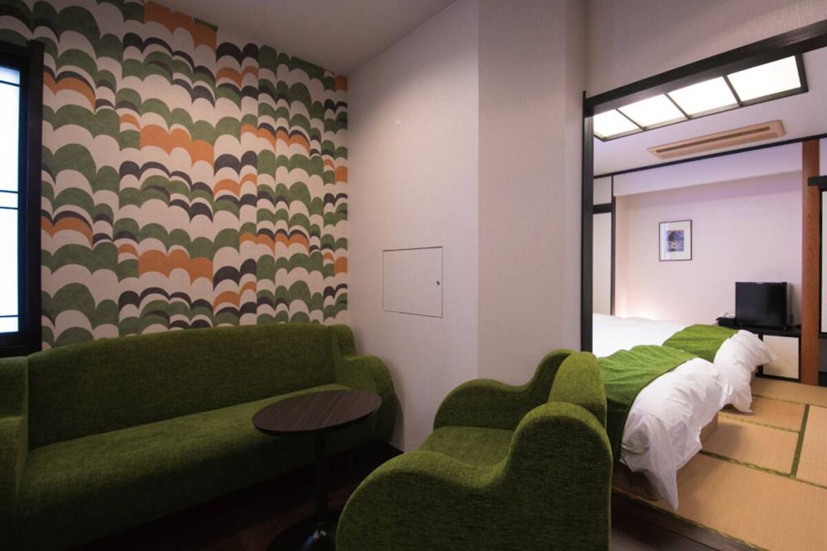 A room with a green sofa, a bed with white bedding, a small table, and a television.
