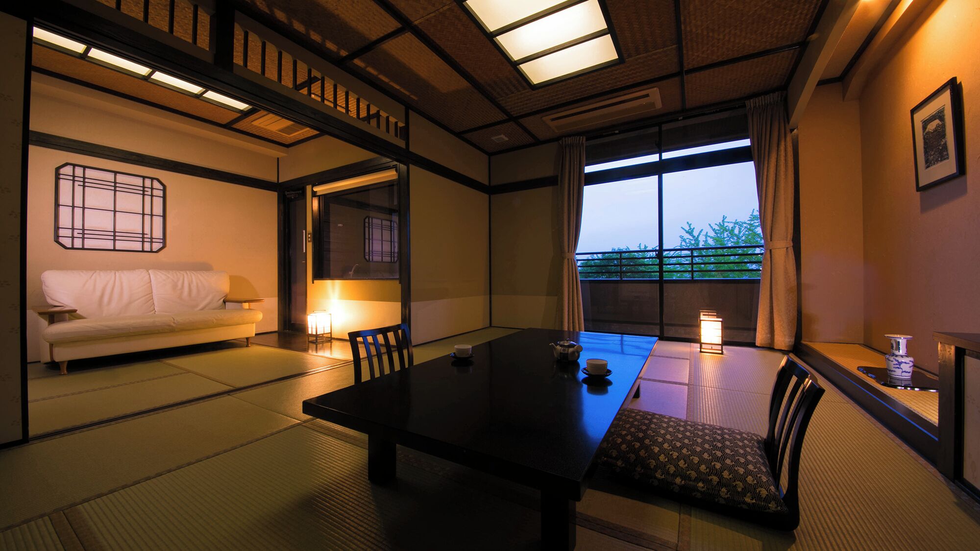 Una habitación japonesa tradicional con suelo de tatami, una mesa baja, un sofá y vistas amplias a través de grandes ventanales.