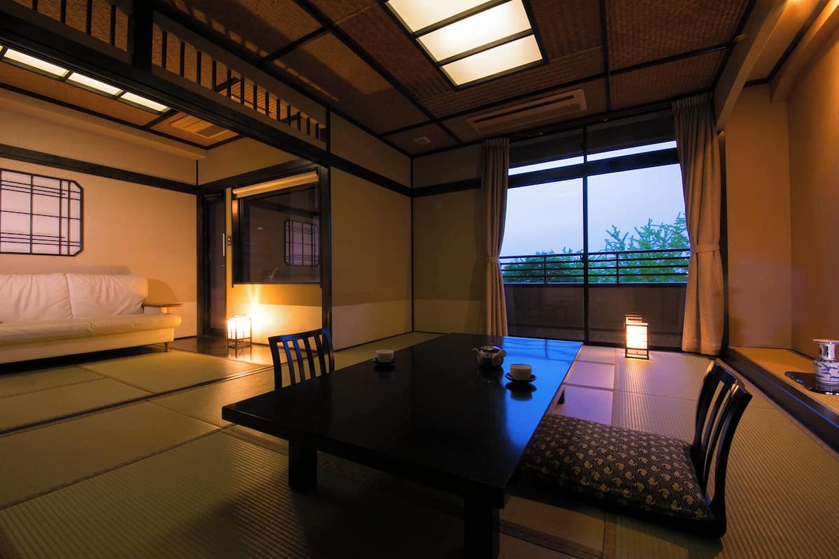 A traditional Japanese room with tatami flooring, a low table, a sofa, and a view through large windows.