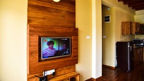 Un salon avec un téléviseur fixé au mur, qui est en bois, un coin cuisine avec des meubles en bois et un réfrigérateur noir.