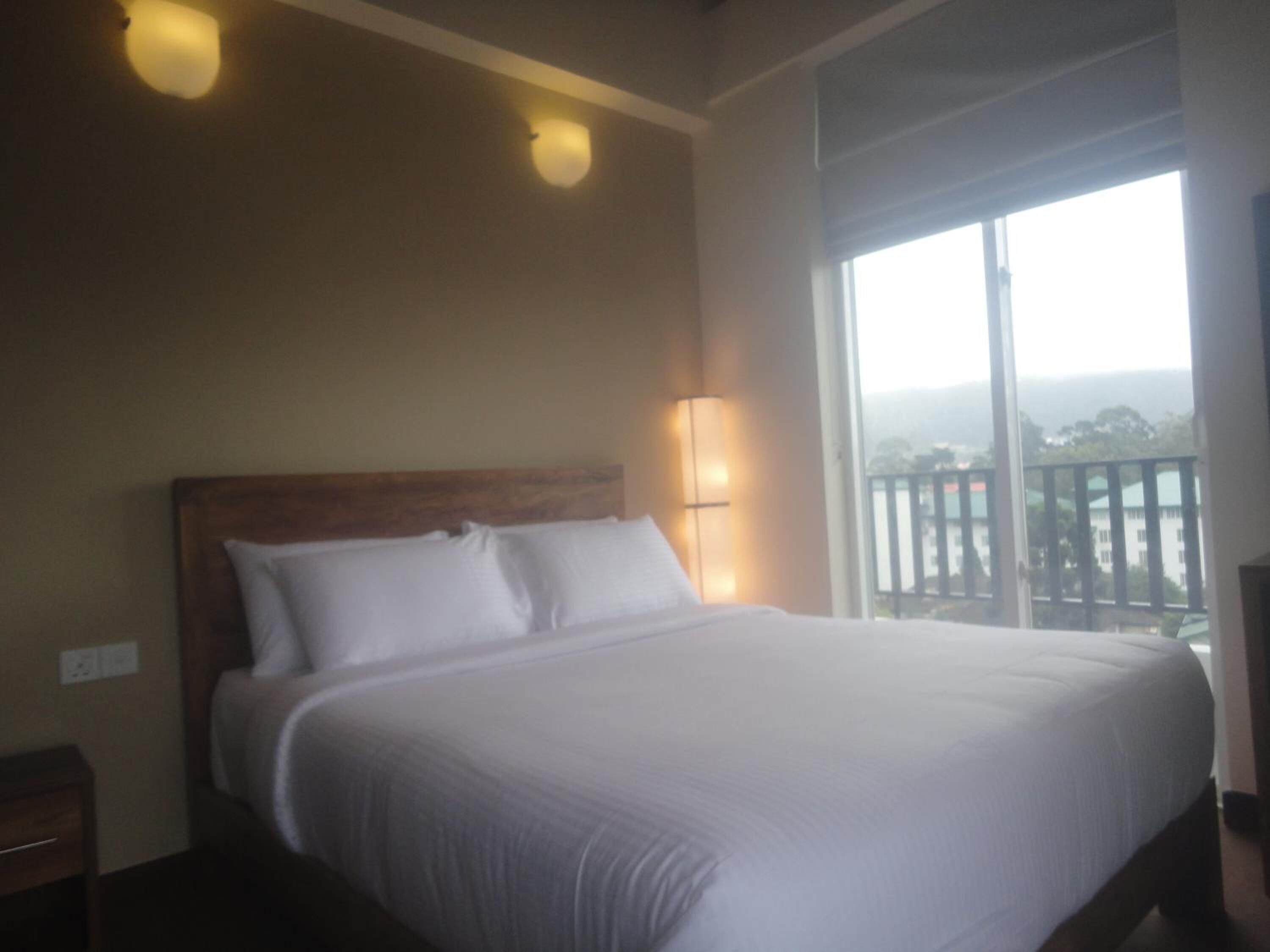 Une chambre d’hôtel avec un grand lit, une table de chevet, une lampe fixée au mur et un balcon avec vue.