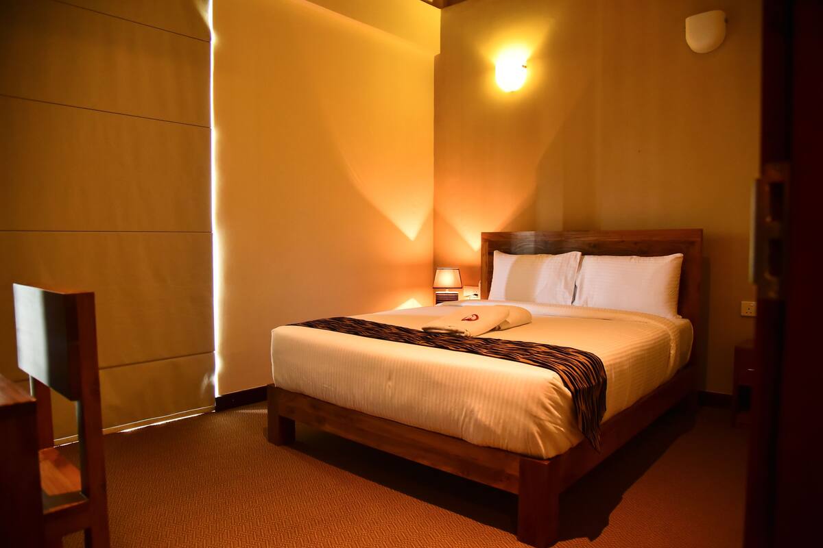Een hotelkamer met een bed, nachtkastje, lamp, stoel en een wandlamp.