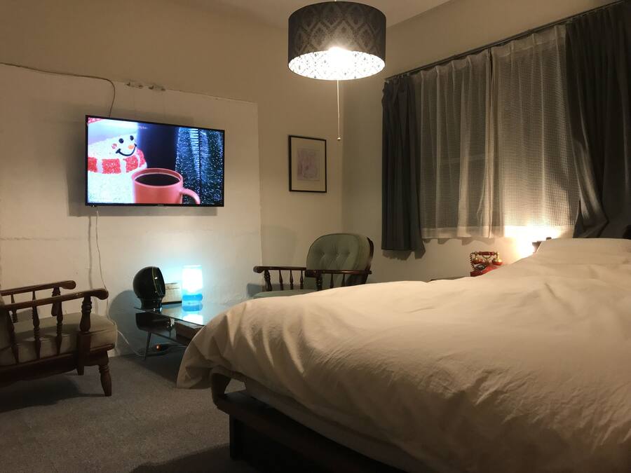 Een slaapkamer met een groot bed, een aan de muur bevestigde televisie, een bureau met lamp en een stoel.