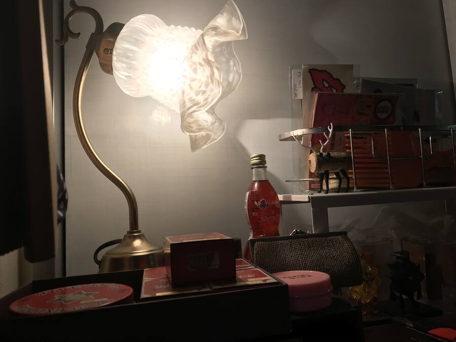 A desk with a lamp, a bottle, and various items on a shelf.