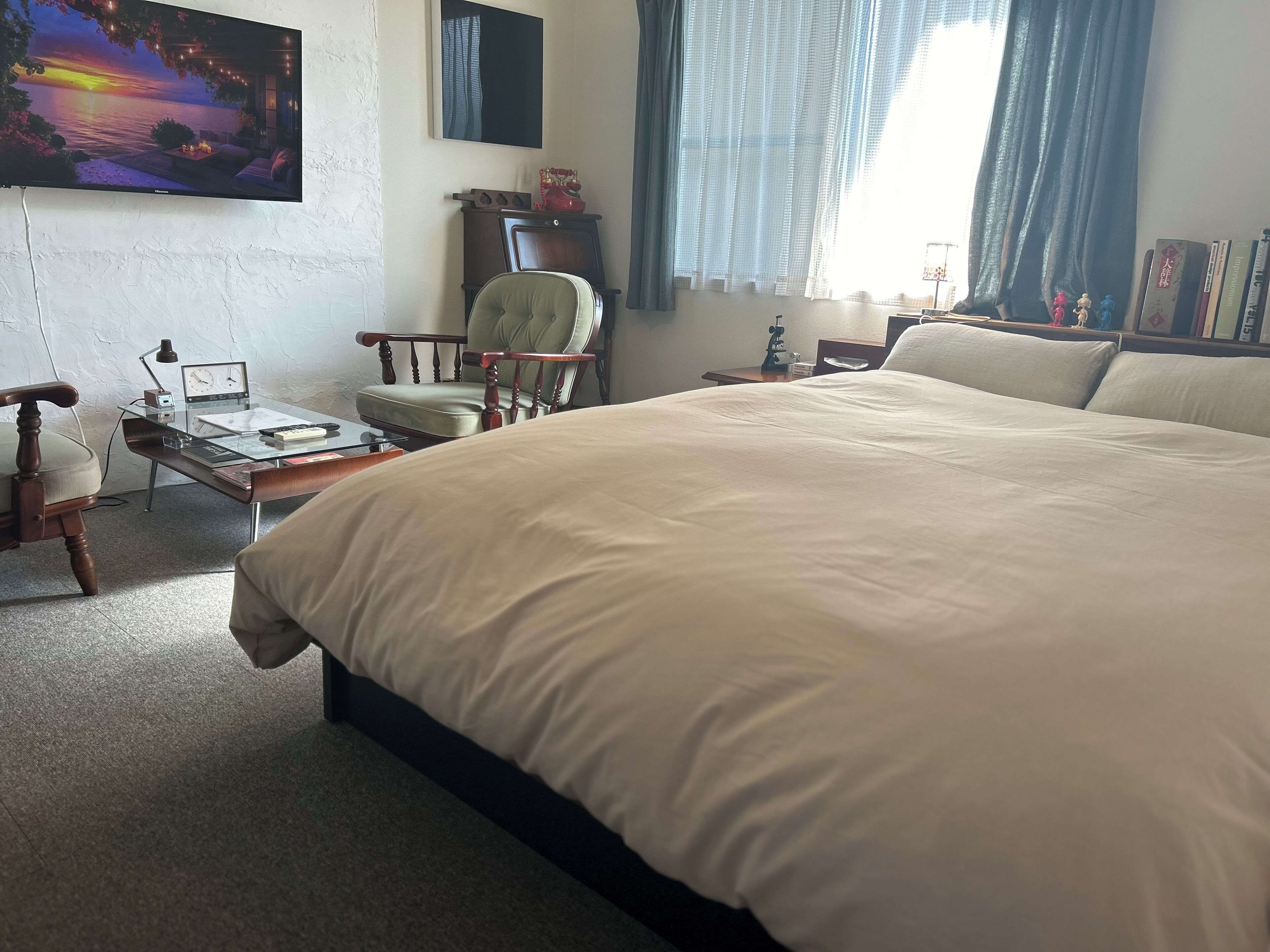 A hotel room with a large bed, a desk with a lamp, a chair, a TV on the wall, and a window with curtains.