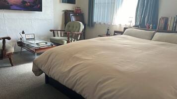 A hotel room with a large bed, a desk with a lamp, a chair, a TV on the wall, and a window with curtains.