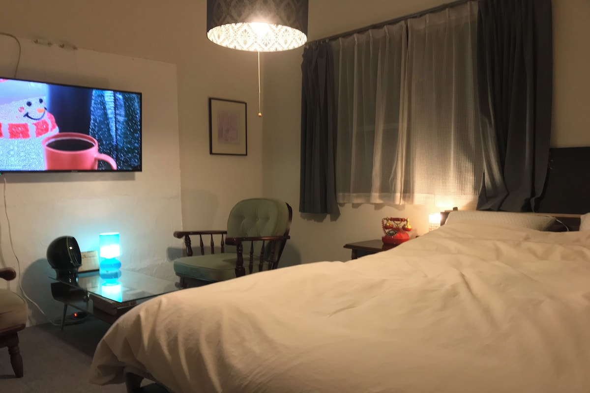A hotel room with a bed, a desk with a lamp, a chair, a television, and a window with curtains.