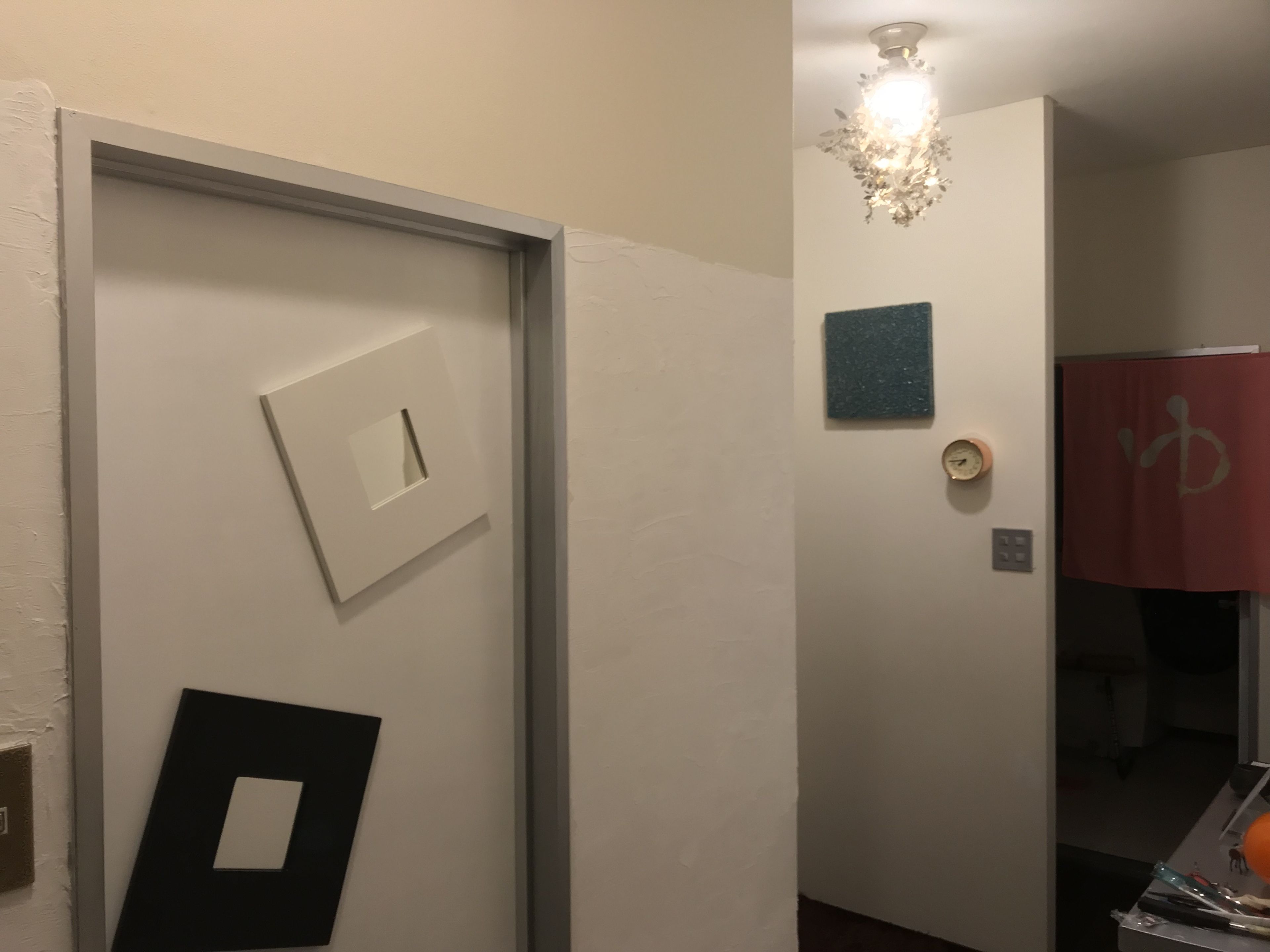 A hallway with a door, a light switch, a small clock, and a red curtain with a symbol.