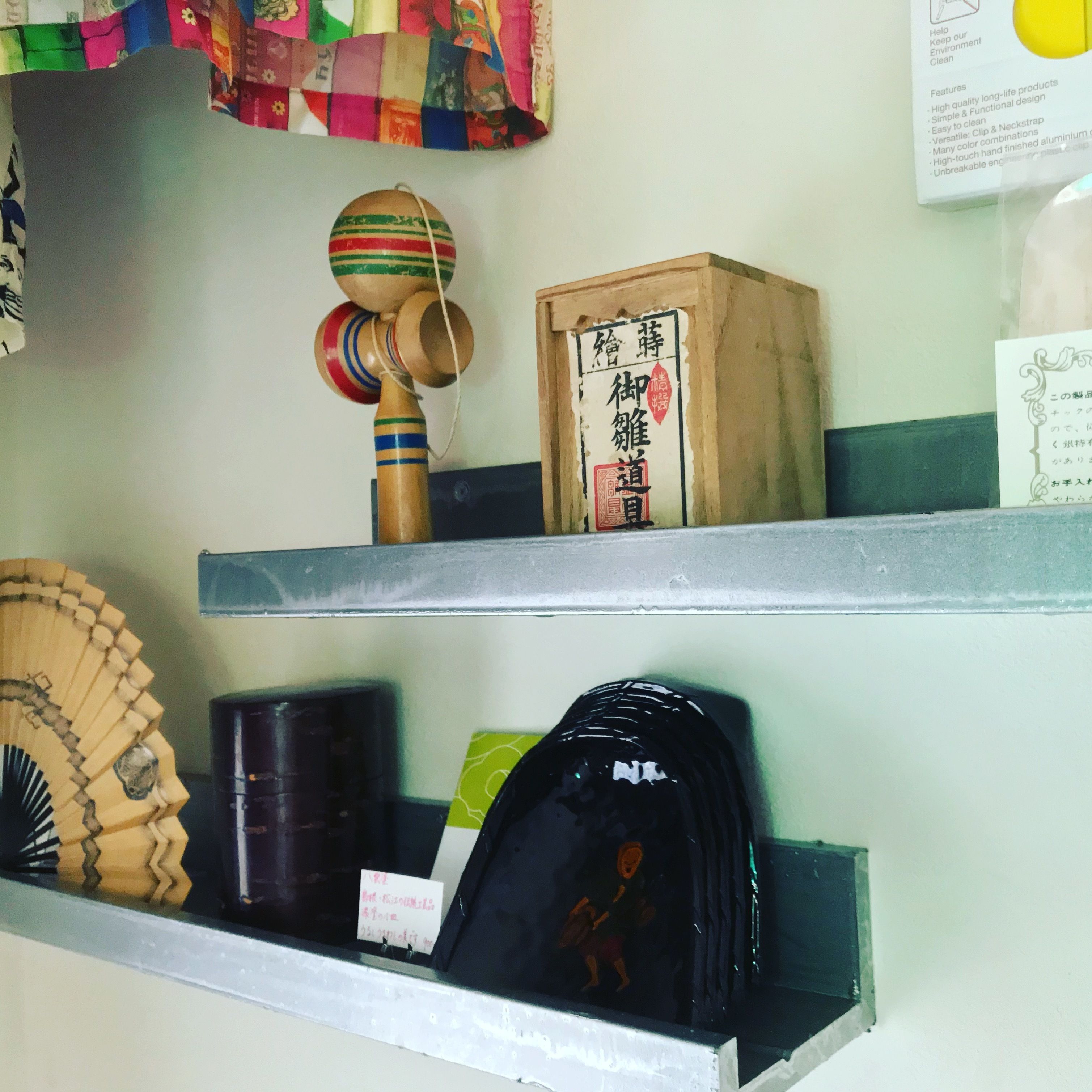 A shelf with a wooden toy, a box with Japanese characters, a fan, and a black bag.