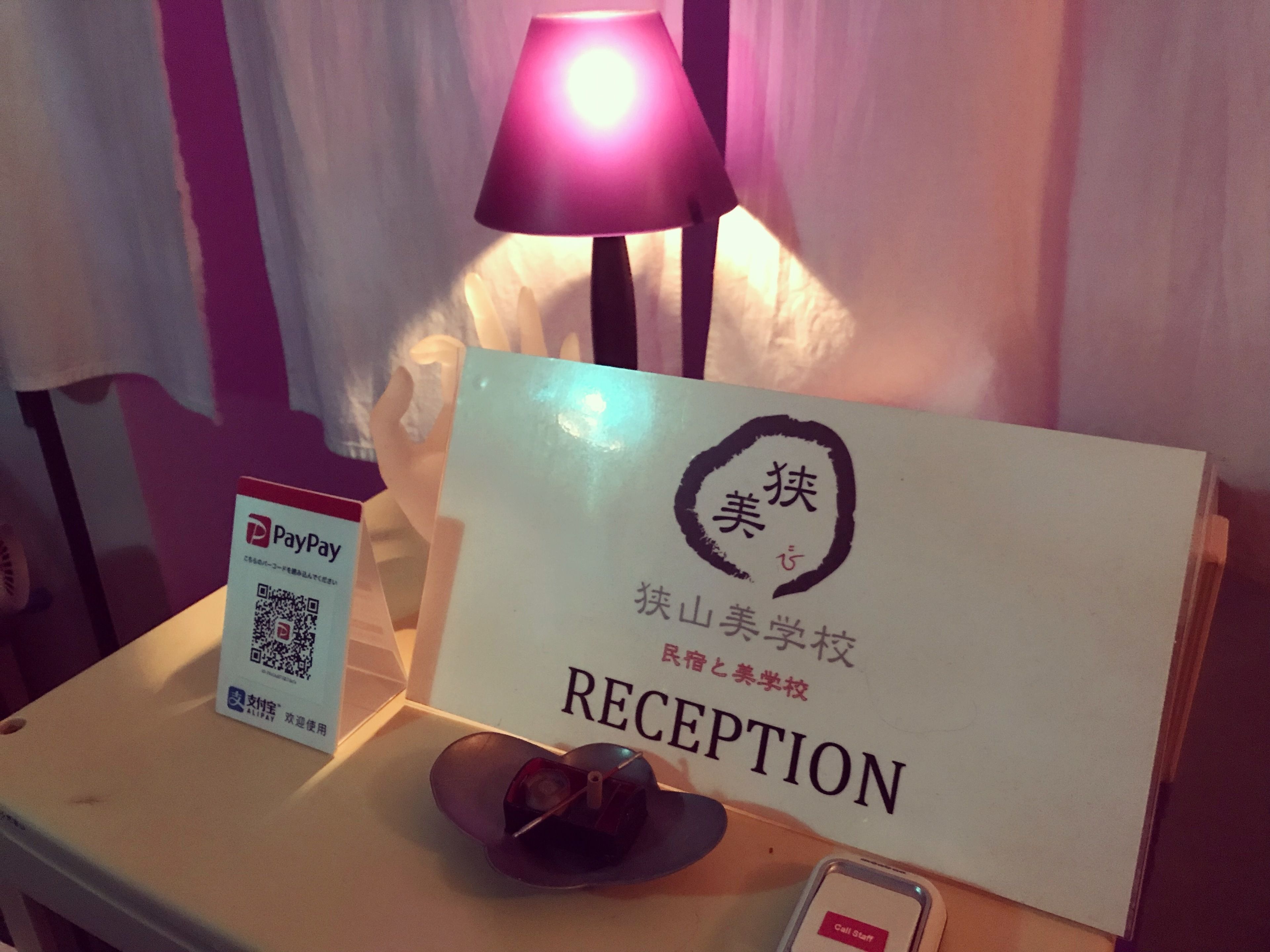 Un mostrador de recepción con un lector de tarjetas PayPay, una lámpara y un cartel con caracteres chinos y la palabra 'RECEPTION'.