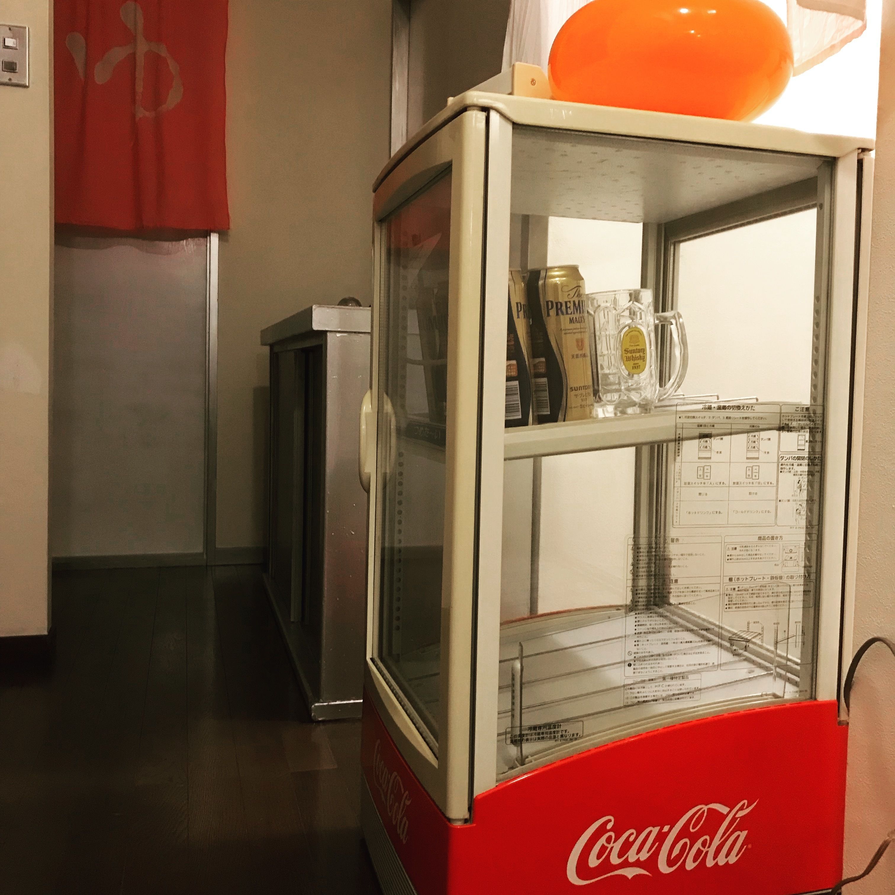 A vending machine with a Coca-Cola logo, containing a bottle and a glass.