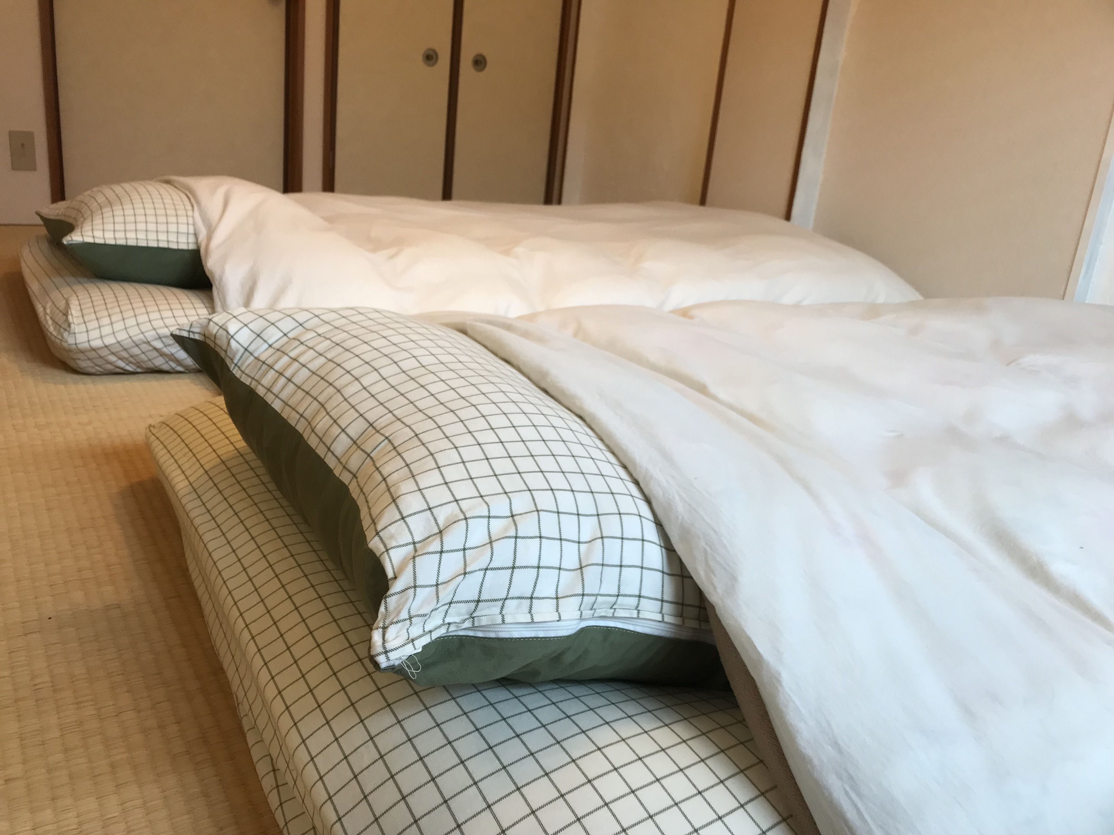 Una cama bien hecha con ropa de cama blanca y un cojín de cuadros.