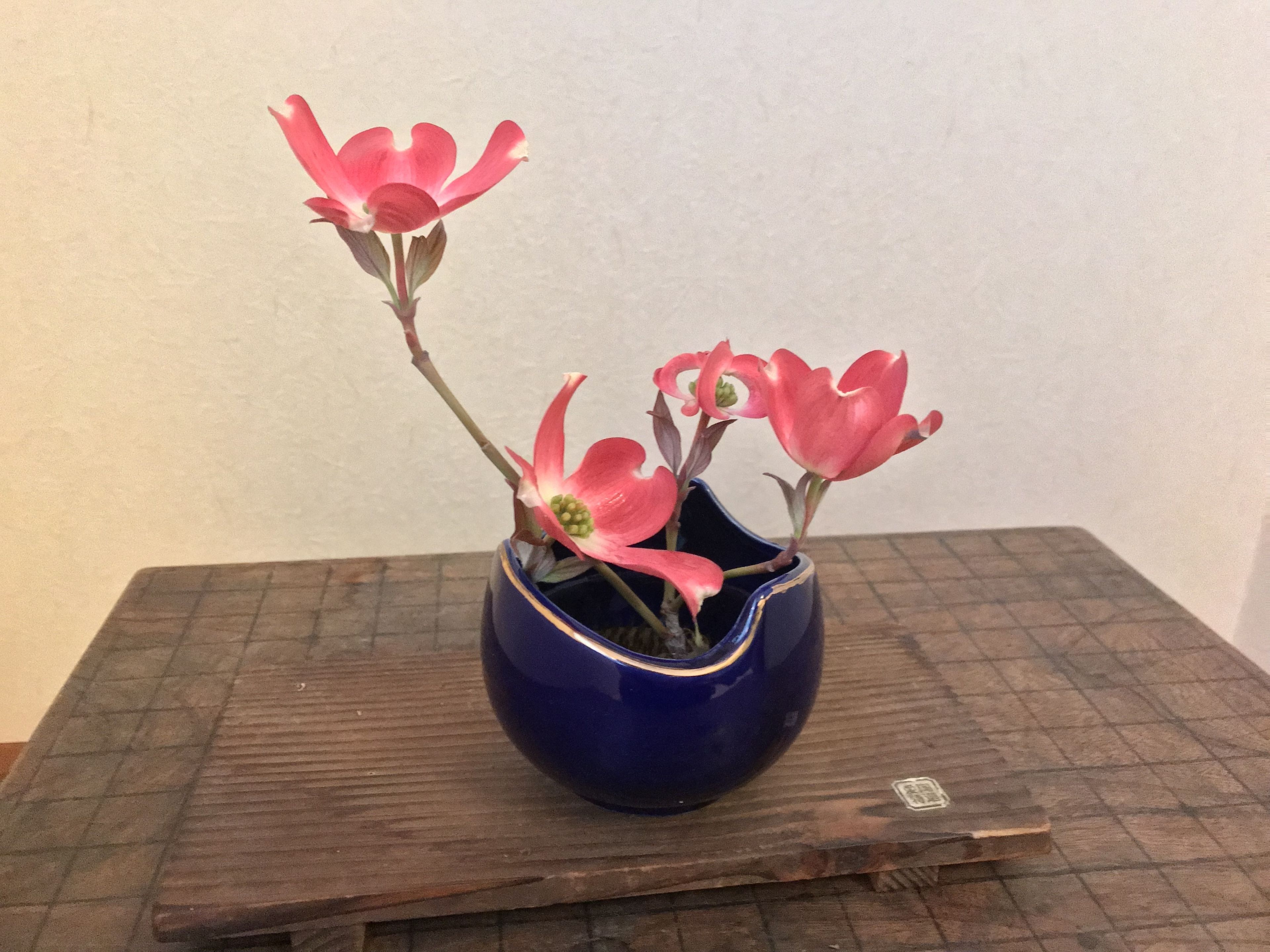A blue vase with pink flowers on a wooden table.