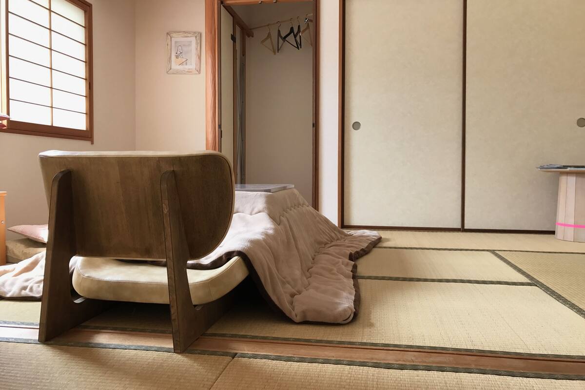 A traditional Japanese room with tatami flooring, a low wooden table, a chair, and sliding doors.