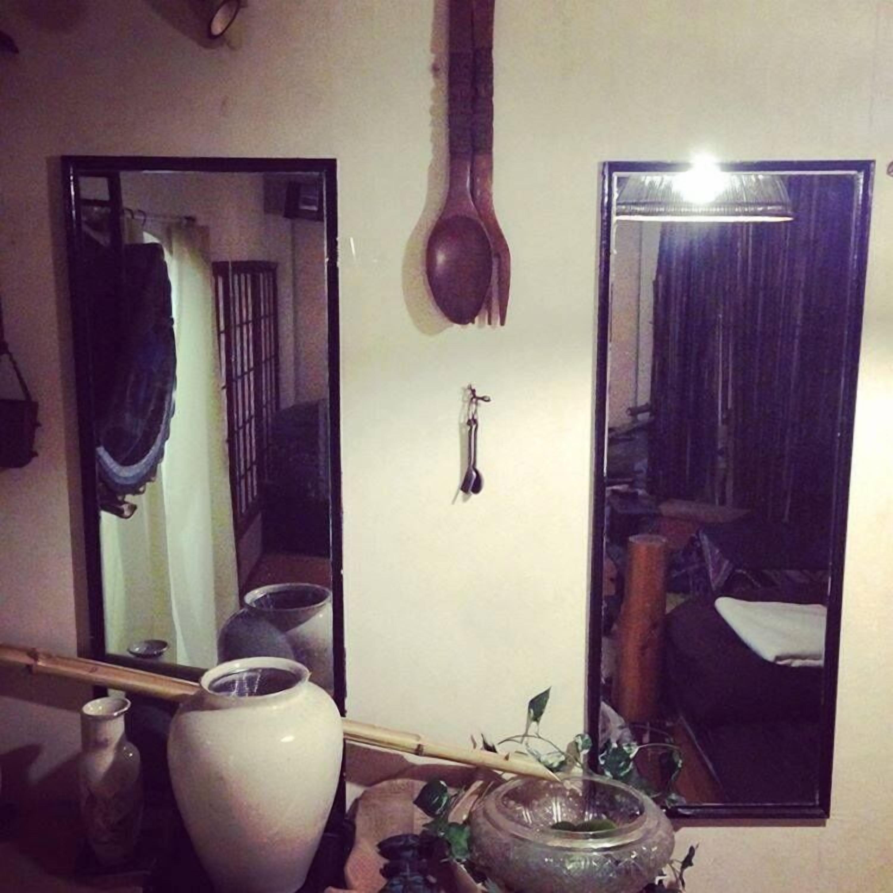 A room with a large mirror, a wooden spoon hanging on the wall, and various containers on a table.