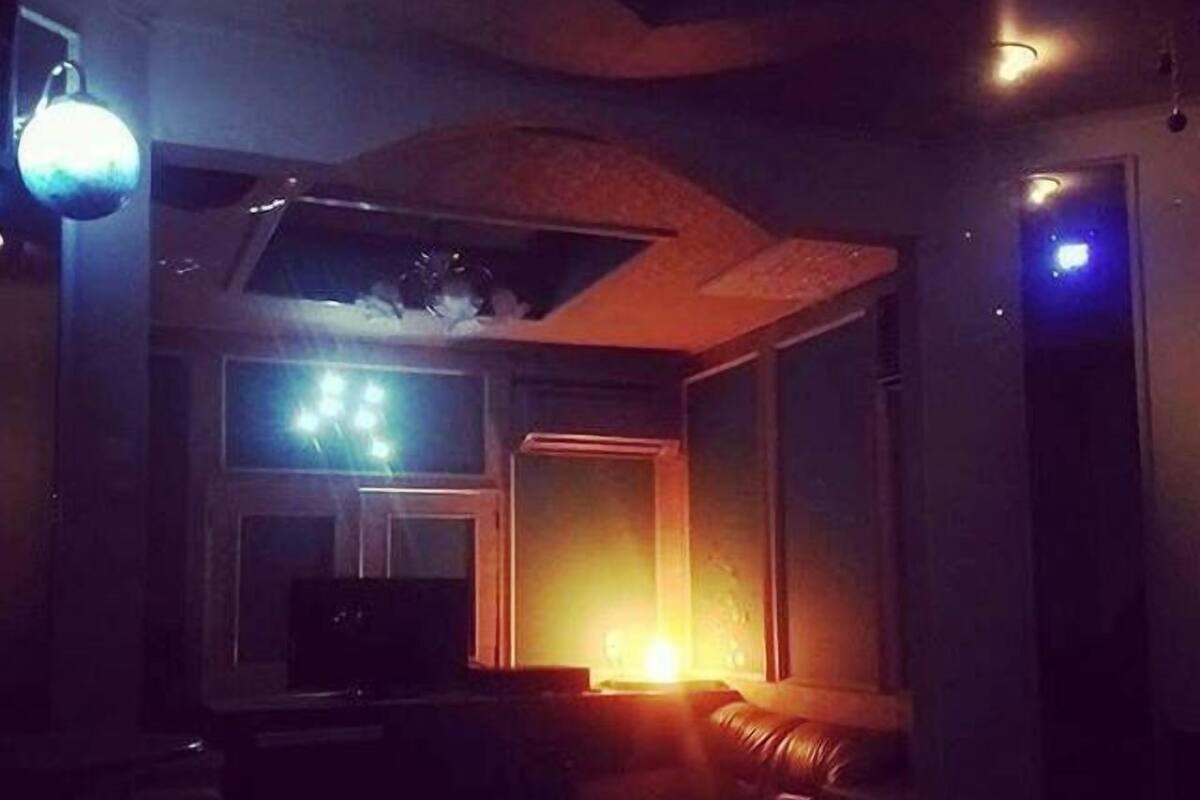 Ett svagt upplyst rum med en lädersoffa, en tv och ett fönster.