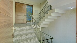 A staircase with a handrail, a wooden door, and a wall-mounted light fixture. - Itsy Hotels Swastika Inn Sector 26 (Noida)