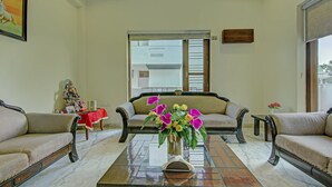 A living room with two sofas, a coffee table with a vase of flowers, a small table with decorative items, and a window with a view. - Itsy Hotels Swastika Inn Sector 26 (Noida)