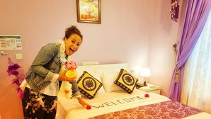 Una camera d'albergo con un letto, un cartello con la scritta 'WELCOME', un comodino con una lampada e un cartello 'NO SMOKING' appeso al muro.