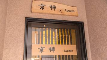 A wooden sign with Japanese characters and the English name "Kyozen" above a window with vertical blinds.