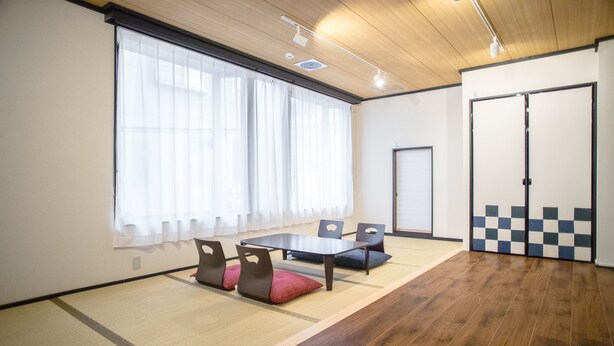 A room with tatami mats, a low table, chairs, and a sliding door. - Guesthouse Kyozen (Kyoto)
