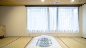 A room with tatami mats, a bed with a patterned pillow, a wooden dresser, and a large window with sheer curtains. - Guesthouse Kyozen (Kyoto)