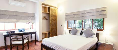 A bedroom with a bed, a desk with a chair, a wardrobe, and a window with curtains.