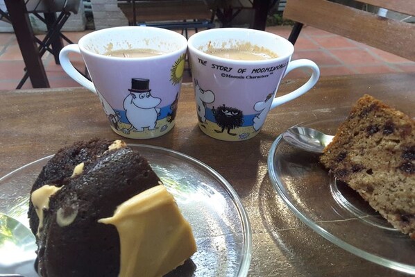 Two mugs with cartoon characters, a slice of cake, and a chocolate dessert on a table. - YK Art House (Phnom Penh)