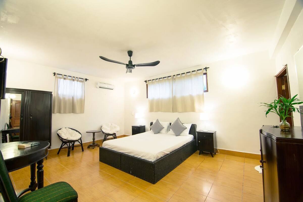A bedroom with a bed, a desk, a chair, a wardrobe, and a ceiling fan.