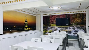 A restaurant with white tables and chairs, a large mural of a cityscape at sunset, and a waterfall scene on the wall. - Bolu Otel (Bolu)
