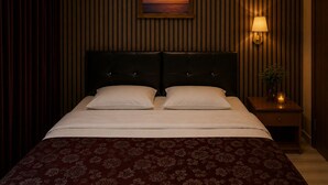 Une chambre d’hôtel avec un lit, une table de chevet avec une lampe, un tableau encadré au mur et une fenêtre avec des rideaux.