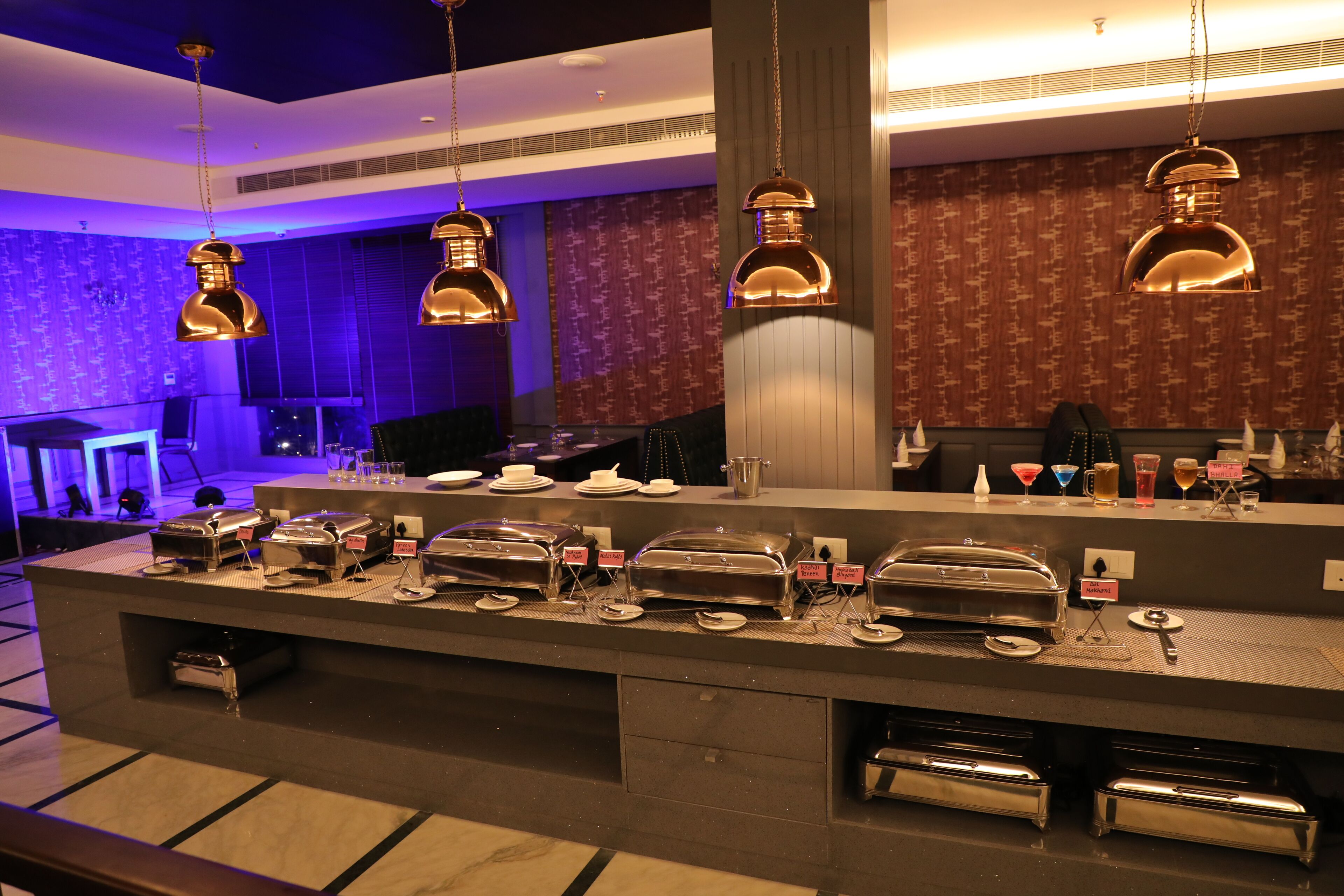 A buffet area with multiple serving stations, a counter with a variety of dishes, and hanging pendant lights.