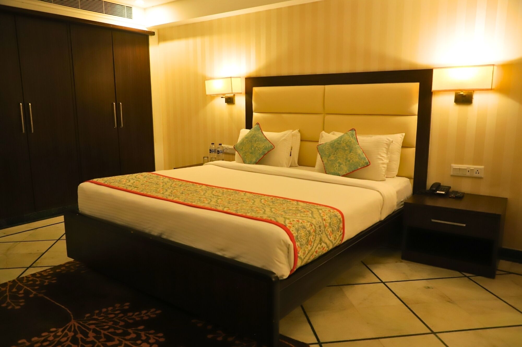 A hotel room with a large bed, bedside tables, a wardrobe, and wall-mounted lamps.