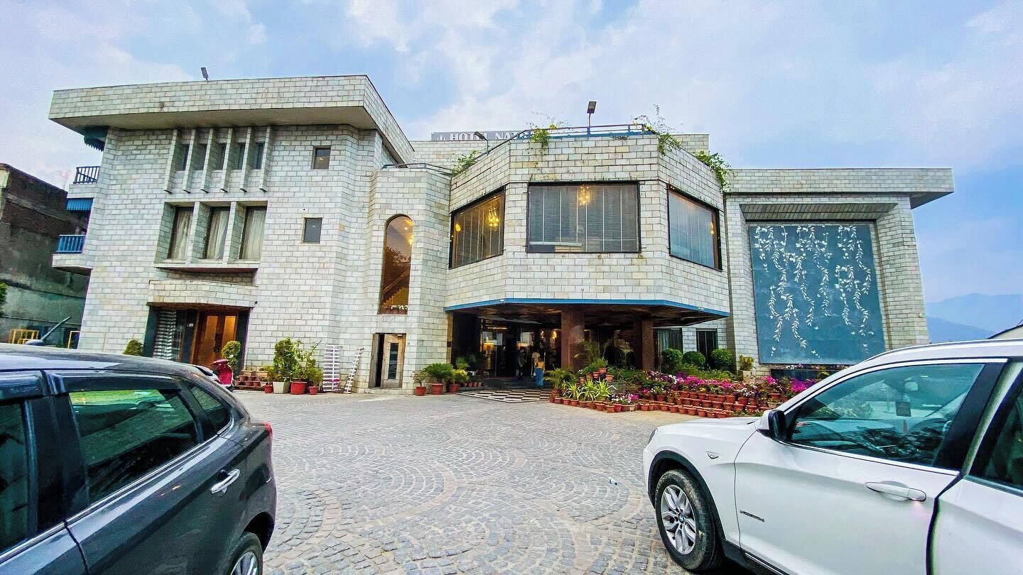 Um hotel moderno com fachada de pedra, entrada coberta e área de estacionamento com dois carros.