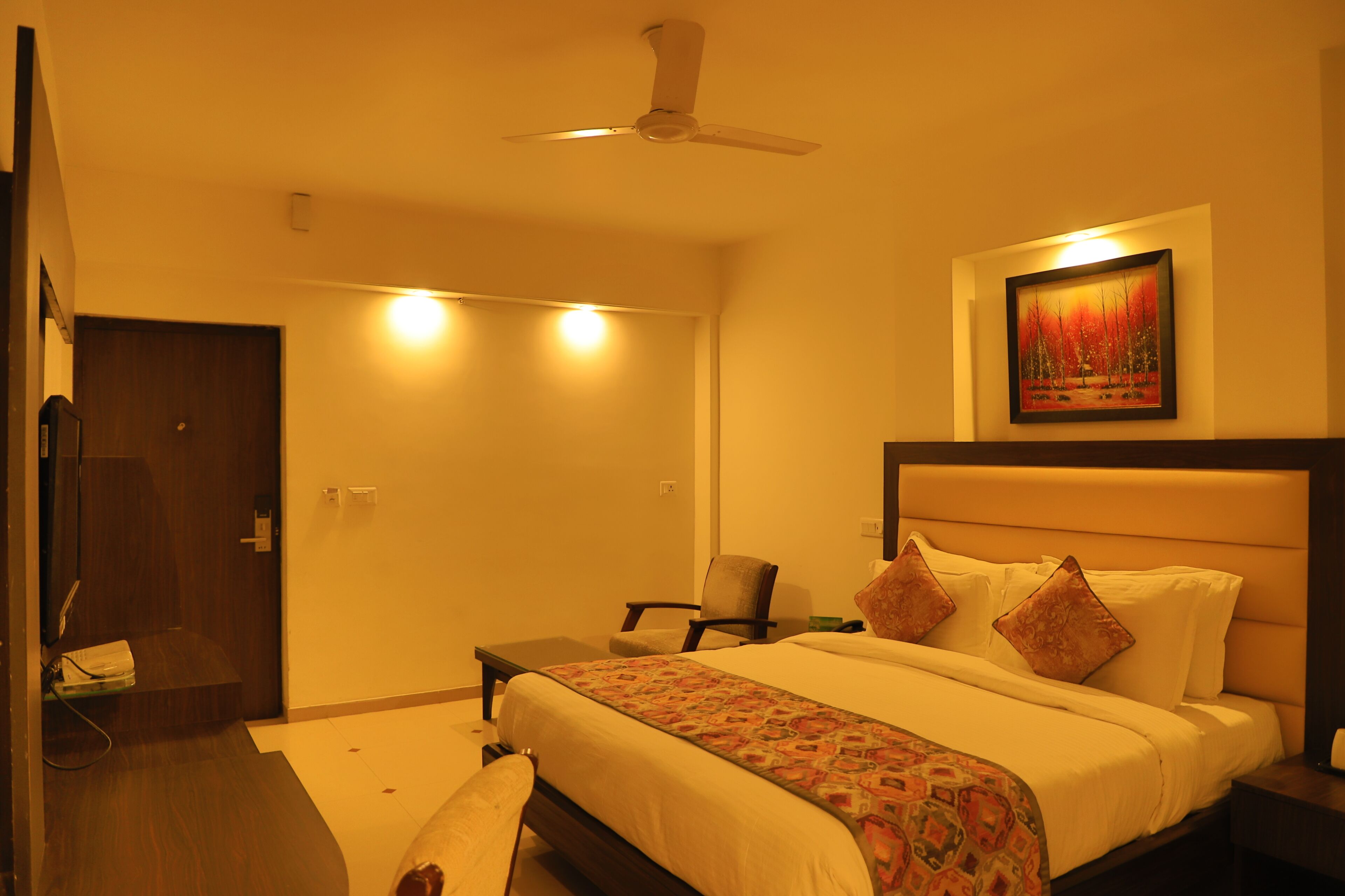 A hotel room with a bed, a chair, a desk, and a painting on the wall.
