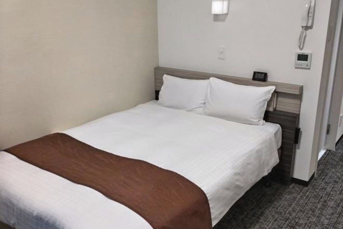 Een hotelkamer met een bed, nachtkastje, telefoon en een thermostaat aan de muur.