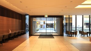 Un hall d’hôtel moderne doté d’un comptoir d’accueil, d’un espace salon et de grandes fenêtres donnant sur la rue.