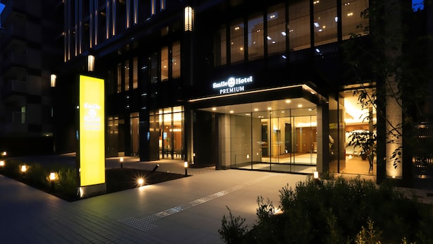 Une entrée d’hôtel moderne avec une façade en verre, un éclairage décoratif et un chemin aménagé.