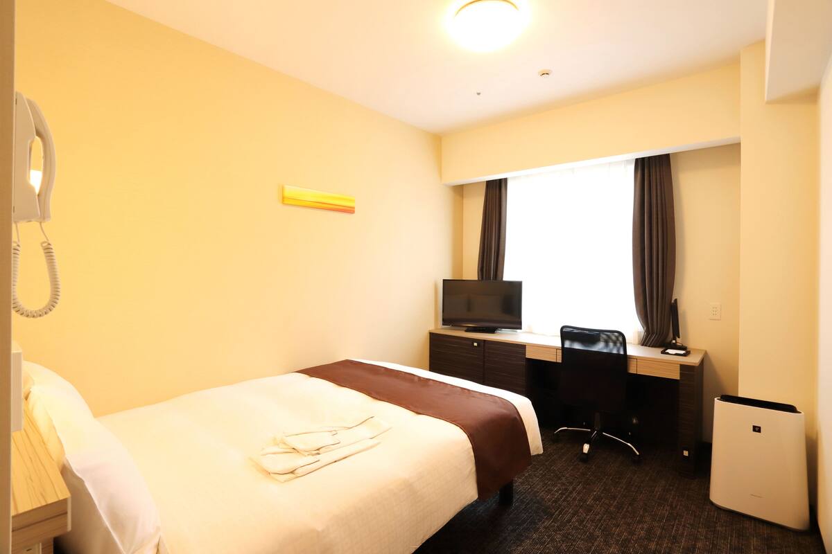Ein Hotelzimmer mit einem Bett, einem Schreibtisch mit Computer, einem Fernseher, einem Telefon und einer kleinen Kühlbox.